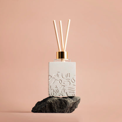Diffuser bottle with decorative design on a rock against a beige background