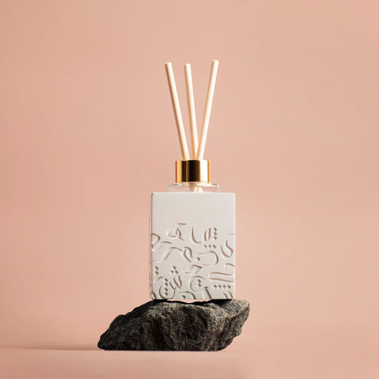 Diffuser bottle with decorative design on a rock against a beige background