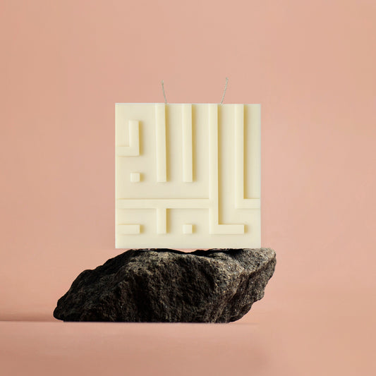 Rectangular white candle with geometric design on a black rock against a beige background